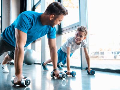 happy father looking at cheerful son and exercising with dumbbells